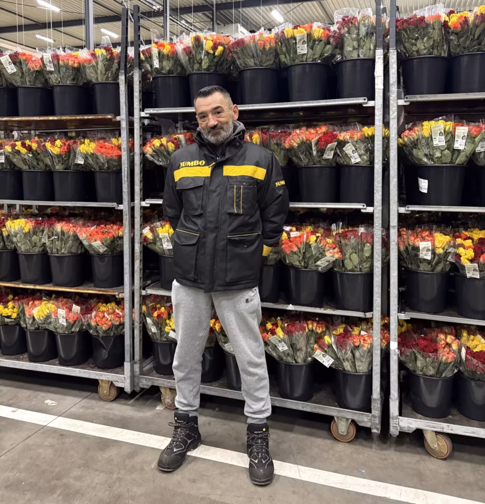 Maciej Bielawski podczas pracy w Jumbo Bloemen en Planten w Veghel, stojący przed regałami z kolorowymi bukietami kwiatów.